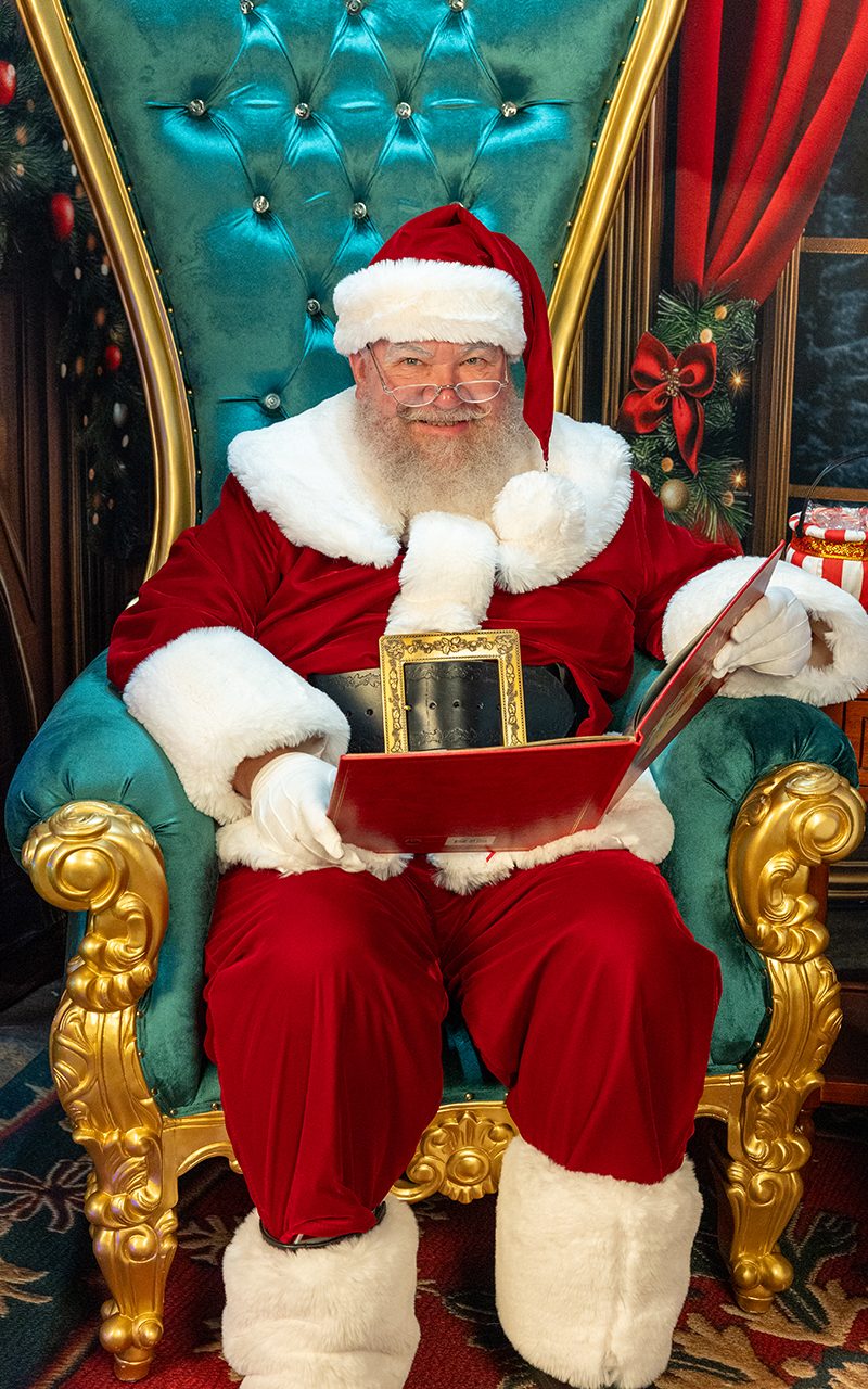 Santa Strickland seated on his throne, reading a Christmas storybook
