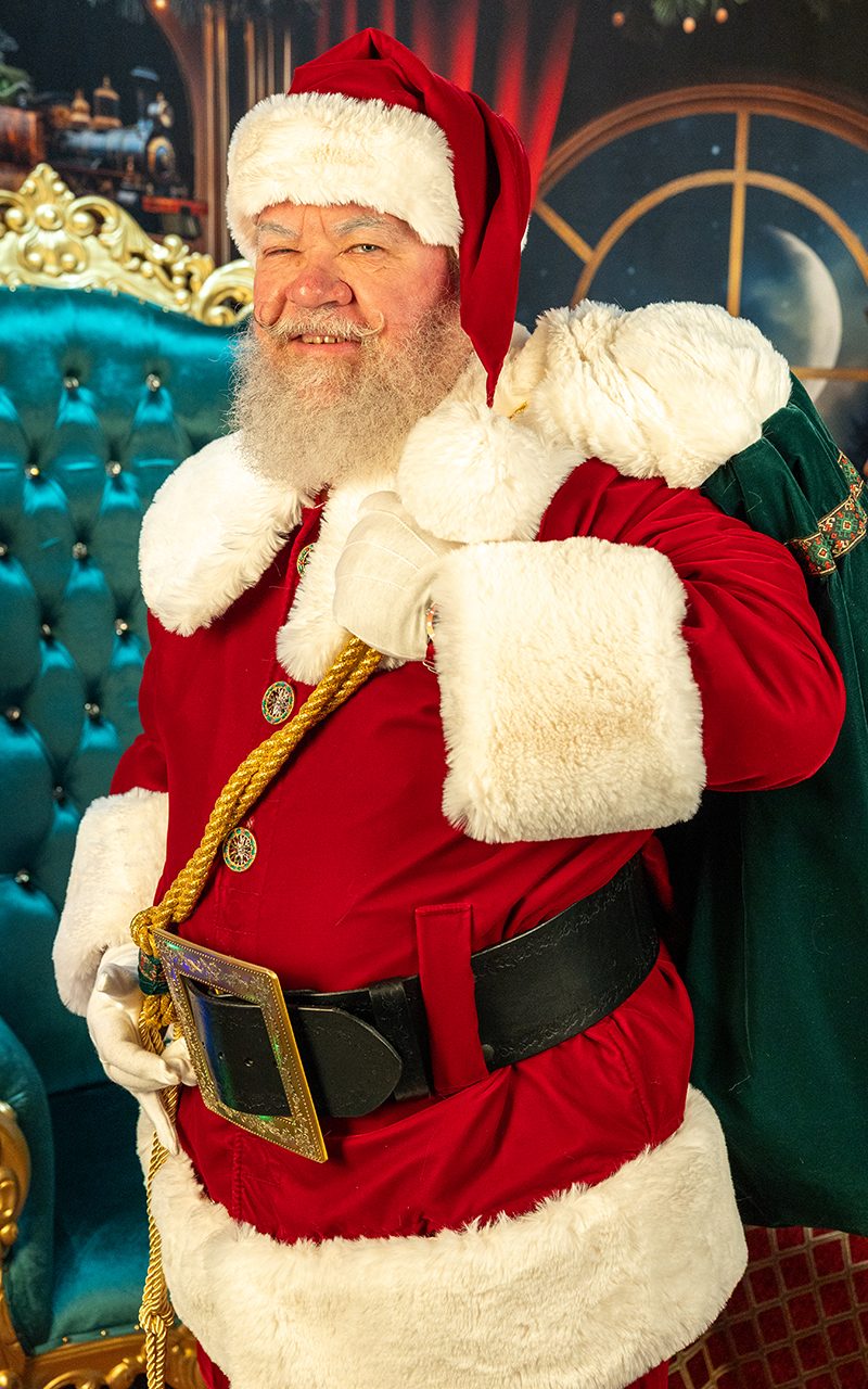 Santa Strickland with a toy sack over his shoulder, giving a cheerful thumbs up
