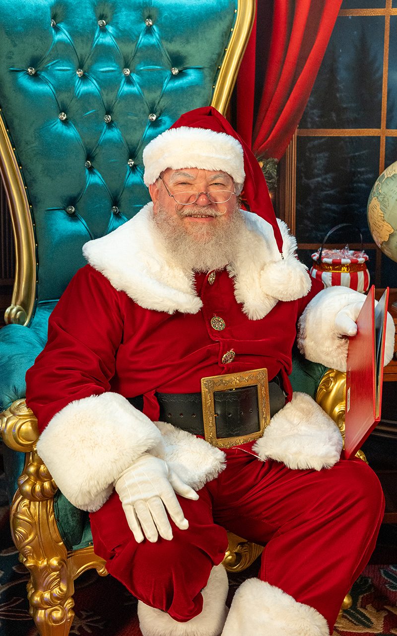 Santa Strickland seated with a warm smile, holding 'The Night Before Christmas'