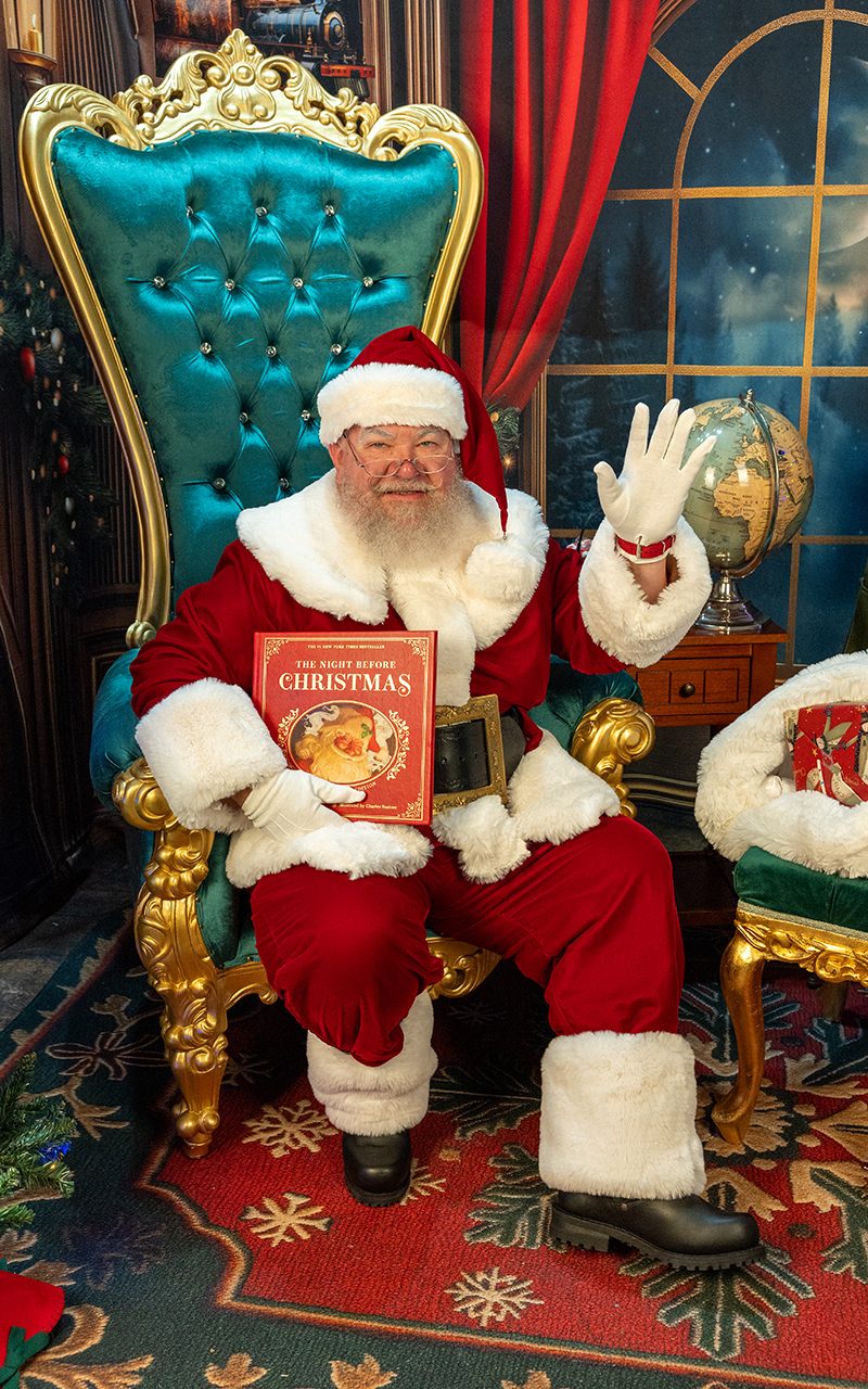 Santa Strickland waving hello from his golden throne, storybook in hand